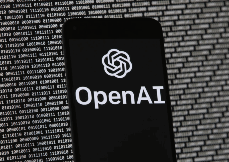 The OpenAI logo appears on a mobile phone in front of a computer screen with random binary data, March 9, 2023, in Boston. (AP Photo/Michael Dwyer, File)